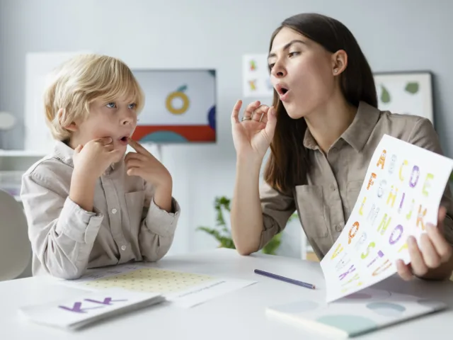 woman doing speech therapy with little blonde boy scaled 1